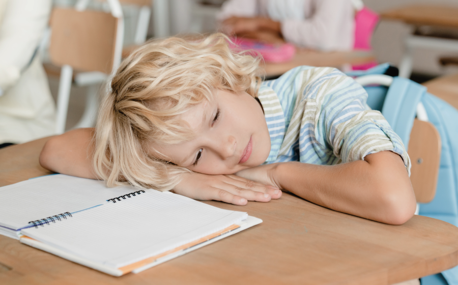 Dziecko znudzone szkolnymi zajęciami, leżące z głową na ławce, cierpiące na ADHD