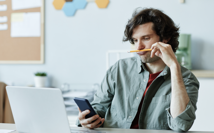 Osoba z ADHD w pracy: mężczyzna w biurze bawiący się ołówkiem i patrzący w telefon